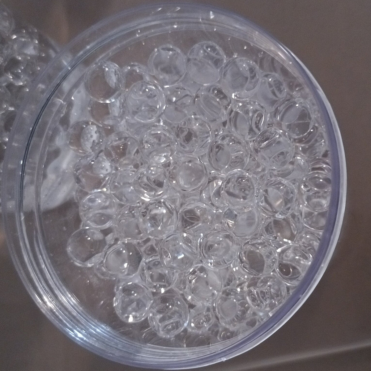 Clear aqua nibble beads in a transparent container on a reflective surface